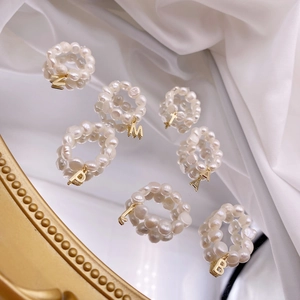 Detail of woven freshwater pearl rings featuring hanging golden metal initial charms