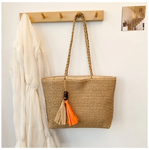 Detail of light brown straw tote bag with colorful wooden beads and orange fringe charms