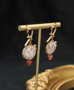 Detail of gold pearl earrings with zircon bow and red heart pendant on black background