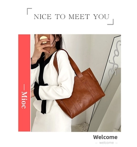 Close-up of brown PU leather tote bag with wide shoulder strap worn by a model