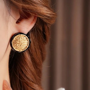 Detailed close-up of golden textured round earrings with black wavy borders on model