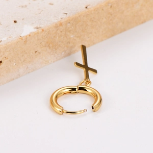 Minimalist stainless steel gold hoop earring with cross pendant on a stone background