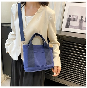 Blue canvas small tote bag with wide shoulder strap styled on a model in white blazer