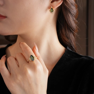 Dettaglio di parure dorata con pietre di zircone verde a pera e accenti di cristallo