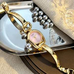 Detail of golden horseshoe bangle watch with pink dial and small pearls on reflective tray