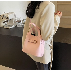 Pink lychee grain leather bucket bag with metal buckle shown in a minimalist cafe
