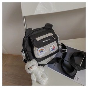Detail of canvas crossbody bag with rainbow badges and a white plush bear pendant