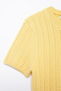 Dettaglio di un top in maglia gialla a maniche corte con motivo a treccia e girocollo a coste