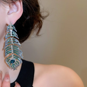 Close-up of luxury leaf feather earrings with blue crystals and emerald rhinestones