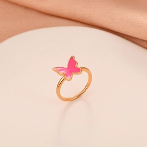 Macro detail of golden butterfly ring with pink enamel on a soft fabric background