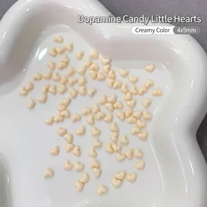 Macro detail of 4x5mm beige resin heart nail charms on a white ceramic plate