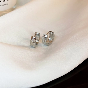 Macro shot of silver hoop earrings with geometric texture on elegant white silk fabric