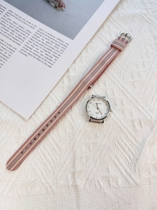 Detail of minimalist quartz watch with pink and grey striped nylon strap on a magazine