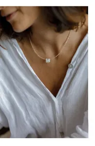 Macro detail of natural shell letter M pendant on a delicate beaded choker necklace