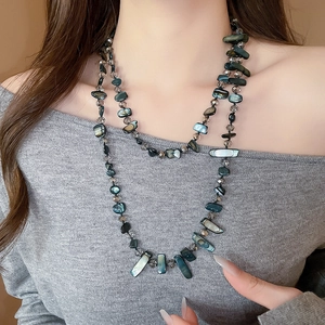 Close-up of double-layered beaded necklace with iridescent shell slices on grey sweater