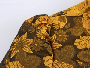 Detailed macro view of dark fabric with gold floral pattern and pleated structure