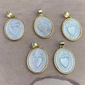 Set of five oval gold necklaces with white mother of pearl Sacred Heart pendants on wood