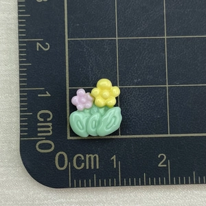 Close-up of mini resin flower charms in yellow and pink on a metric scale cutting mat