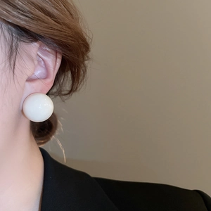 Close-up of white spherical resin stud earrings worn on ear with minimalist style