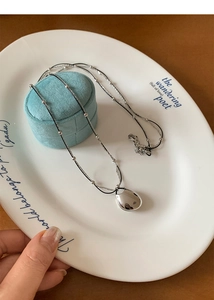 Close-up of a silver water drop pendant necklace on a ceramic plate with velvet box