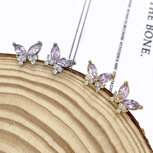 Macro detail of butterfly stud earrings with purple zircons on rustic wood slice base