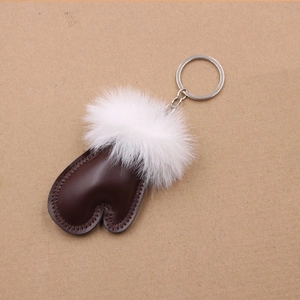 Close-up of brown leather glove pendant with white plush fur ball and metal keychain
