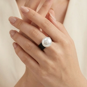 Detail of wide black band ring featuring a large white pearl on a model hand