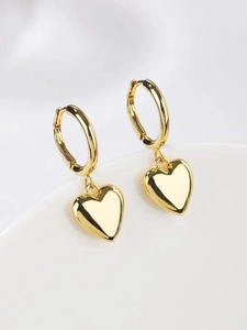 Macro detail of high-polish gold hollow heart pendant earring on white porcelain edge