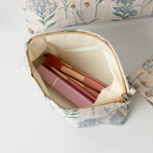 Dettaglio del ricamo floreale su borsa da trucco in tela con cerniera dorata e fodera
