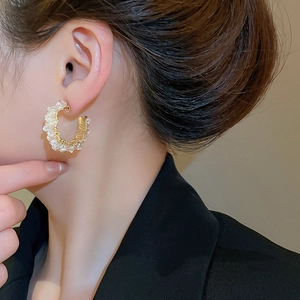 Detailed close-up of C-shaped gold wire earrings with sparkling crystals worn by a model