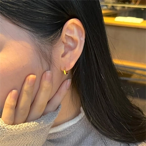 Close-up of a model wearing small golden hexagonal hoop earrings in 925 silver