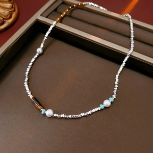 Detail of silver blocks, white pearls and tiger eye beads on a brown jewelry tray