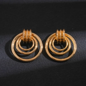 Detailed close-up of golden geometric hollow hoop earrings on a black textured background