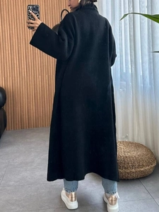 Vue arrière d'un long manteau en maille noir montrant sa coupe élégante et sa longueur