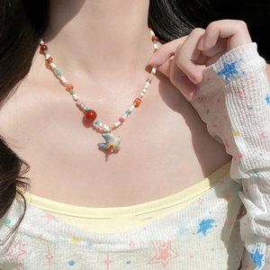 Colorful handmade beaded necklace with blue and white bird pendant worn by a model