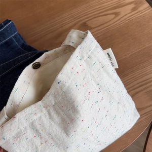 Detailed macro of cream canvas fabric with multicolored speckles and bronze metal snap button