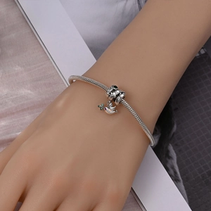 Macro detail of silver snake chain bracelet with olive peace dove and zircon charms