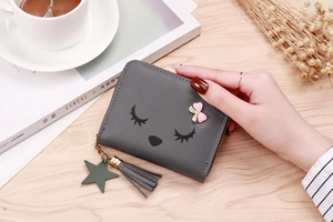 Detail of dark grey coin purse with cartoon face, pink bow, and matching tassel charm