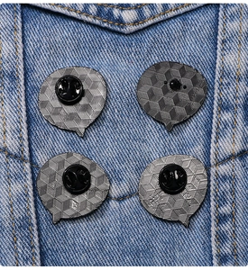 Detailed close-up of four metal pin badges with butterfly clutch backings on denim fabric