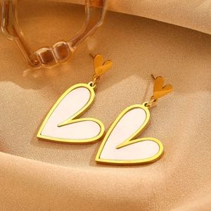 Detailed macro of gold heart earrings with white inlay on a silk fabric background