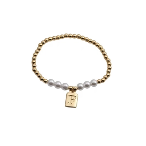 Detail of gold beaded and white pearl bracelet with engraved letter F square pendant
