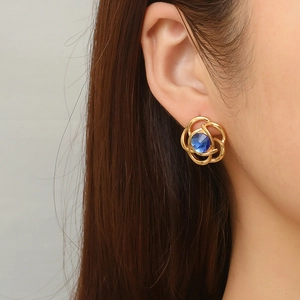 Gold flower stud earring with blue center stone on model, 18K gold plated stainless steel