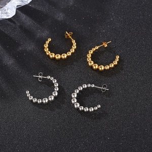 Golden and silver C-shaped bead earrings in stainless steel on a black textured background
