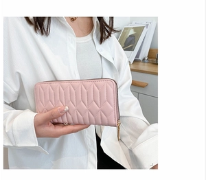 Detail of pink quilted long wallet with gold zipper held by a lady in white shirt