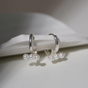 Elegant S925 silver hoop earrings featuring white pearls on a minimalist stone display