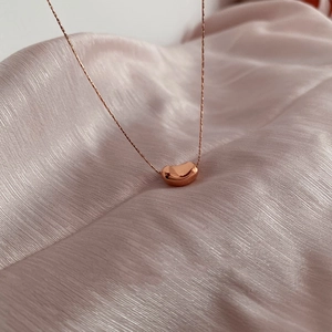 Close-up of a polished rose gold bean pendant on a delicate chain over pink silk