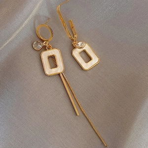 Macro detail of asymmetric gold tassel earrings with shell-like square and zircon stones