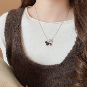 Gros plan du collier pendentif teckel et fleur sur un mannequin portant un pull marron doux
