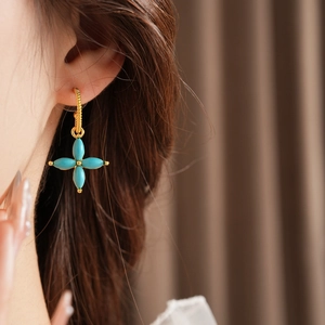 Detail of gold-plated clover earrings featuring four green turquoise drop stones on model