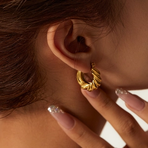 Polished gold-plated stainless steel twisted hoop earrings worn by a model